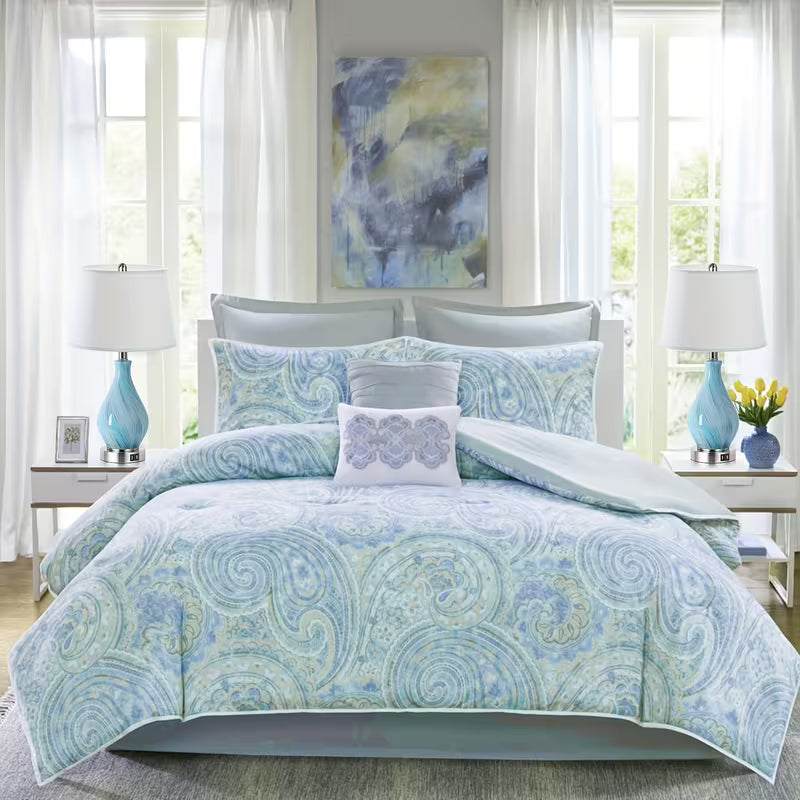 Blue and white patterned comforter set on a bed in a bright bedroom with lamps and artwork.
