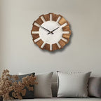 Wooden wall clock on a neutral wall with decorative pillows below.