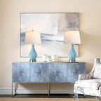 Two table lamps with blue glass bases and white lampshades on a wooden surface.