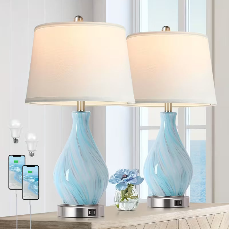 Two table lamps with blue glass bases and white lampshades on a wooden surface.