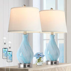 Two table lamps with blue glass bases and white lampshades on a wooden surface.