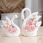 Two decorative swan figurines with floral details on a marble surface.