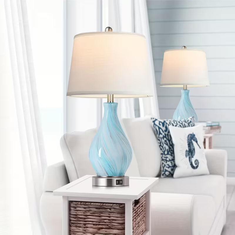 Two table lamps with blue glass bases on a white side table in a living room setting.