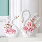 Two decorative swan figurines with floral designs on a white surface.