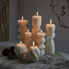 Set of white textured candles on a decorative tablecloth with a branch in the background.