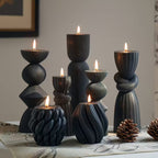 Set of black textured candle holders with lit candles on a table.